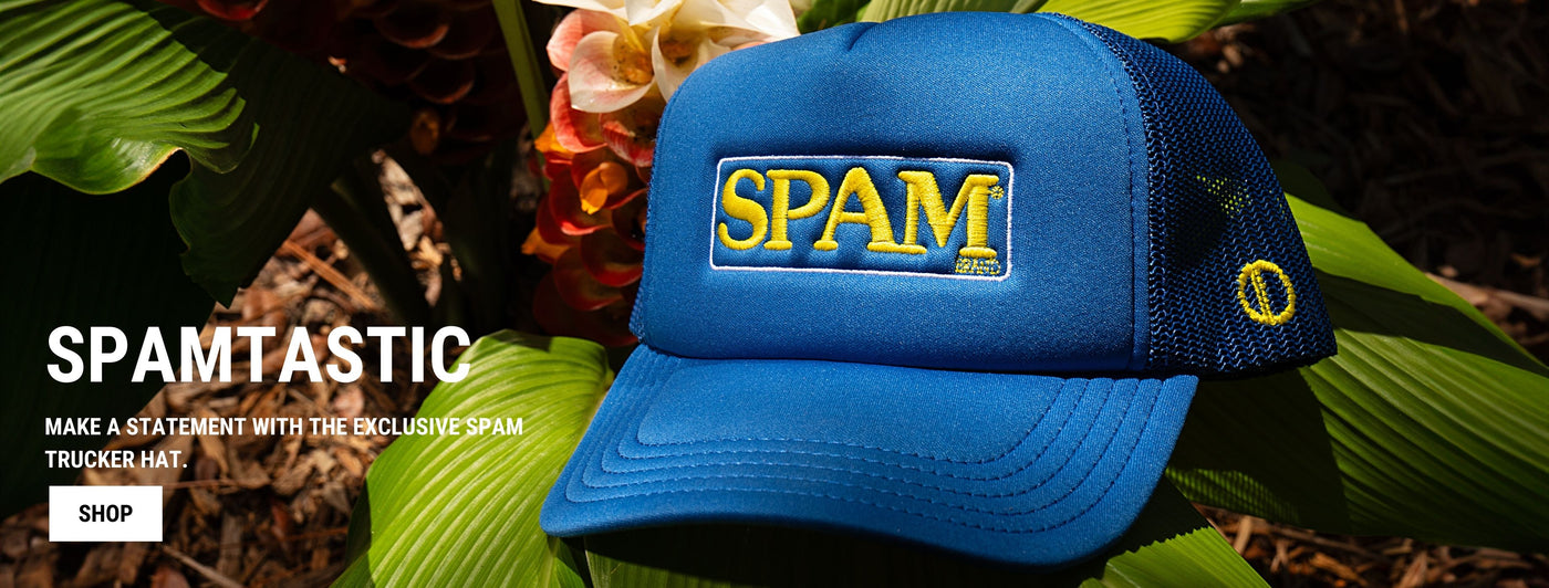 A blue trucker hat with the yellow and blue SPAM logo displayed prominently on the front. The hat is placed on green leaves and vibrant red flowers in the background. The banner text reads "SPAMTASTIC" and "Make a statement with the exclusive SPAM trucker hat." A "SHOP" button is below the text.